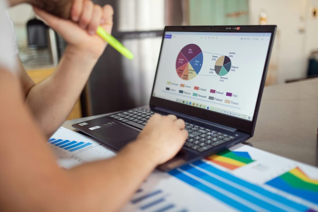 About Us Person analyzing financial charts and graphs on a laptop with colorful documents, showcasing market analysis.